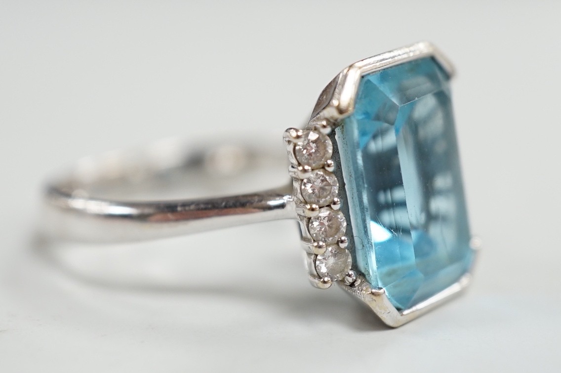 A 750 white metal and emerald cut blue topaz set dress ring, with diamond chip set borders, size O, gross weight 7.8 grams.